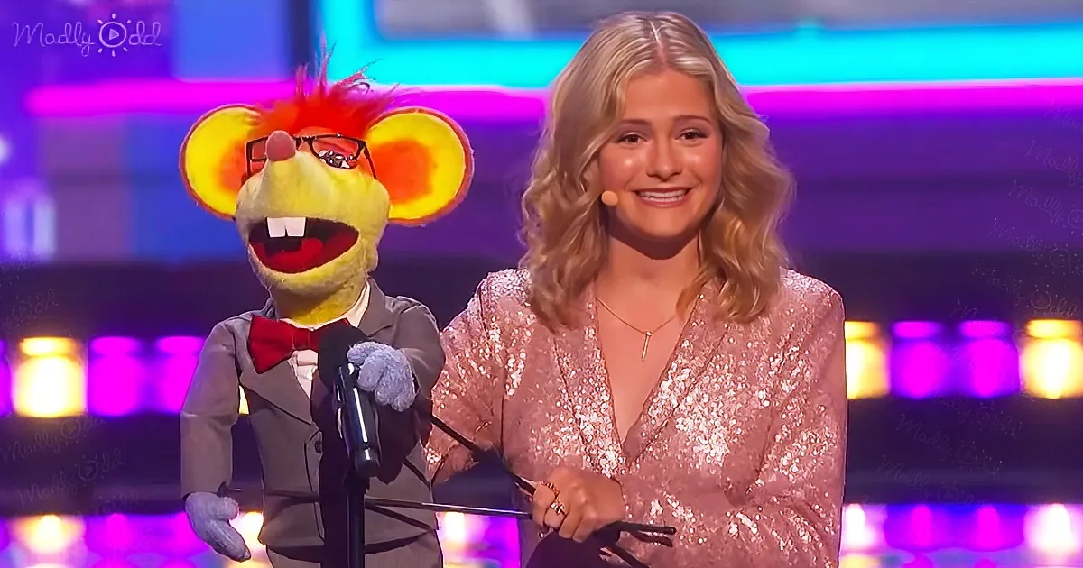 A puppet in a suit and bow tie stands beside a woman in a sparkly dress on a stage.