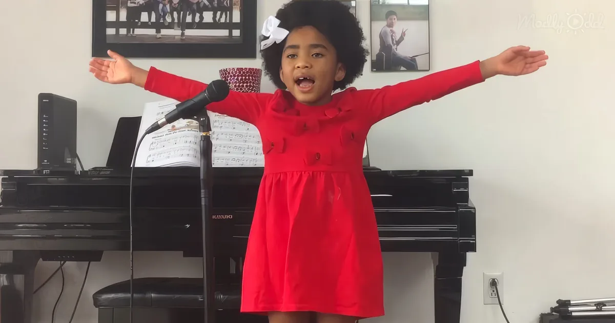 A young girl in a red dress sings passionately with arms outstretched in front of a piano.