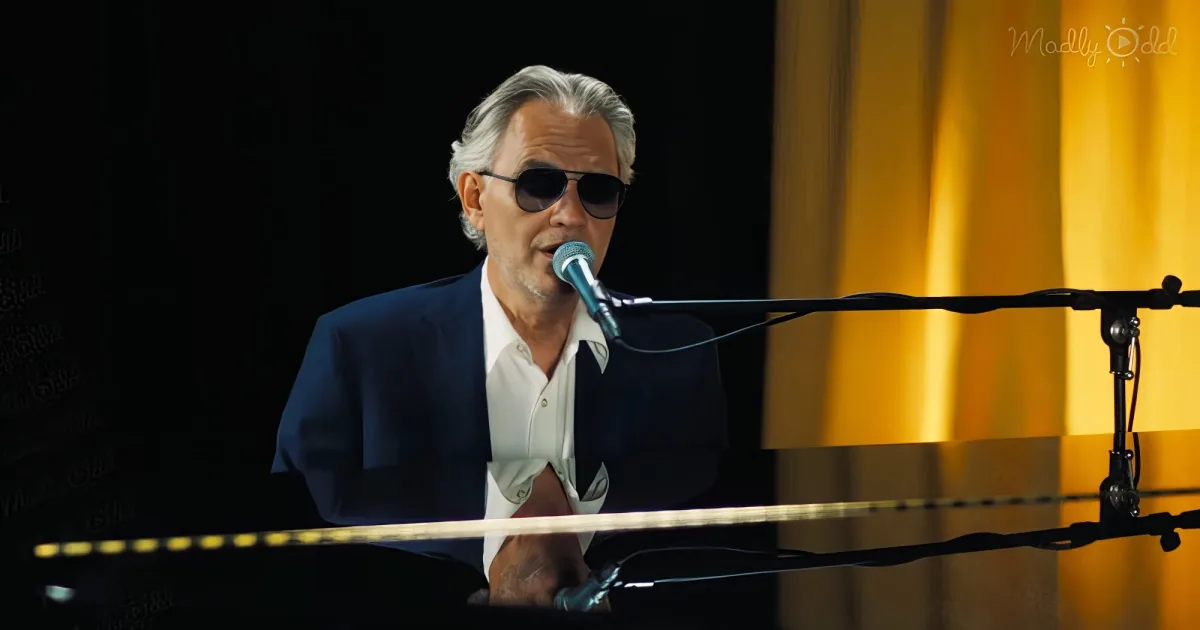 A man in a suit and sunglasses sings into a microphone while playing piano.