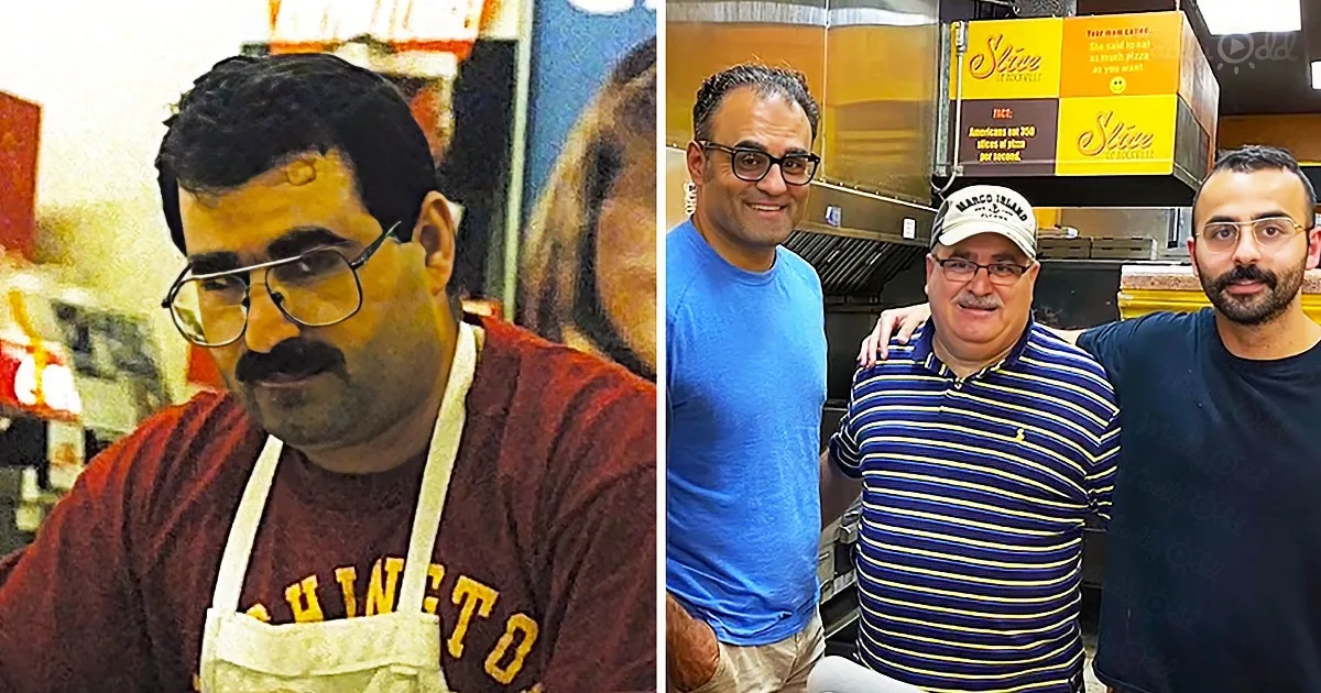 A man in a red shirt and apron stands in a kitchen, smiling, with another group of men in the background.
