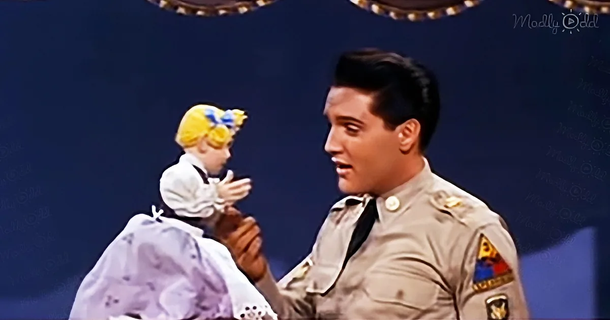 Elvis Presley in a police uniform holds a baby doll on stage.