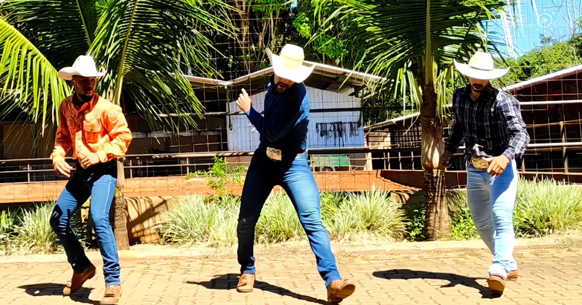 A man in a cowboy hat and jeans is dancing on a brick patio, with palm trees and a building in the background.