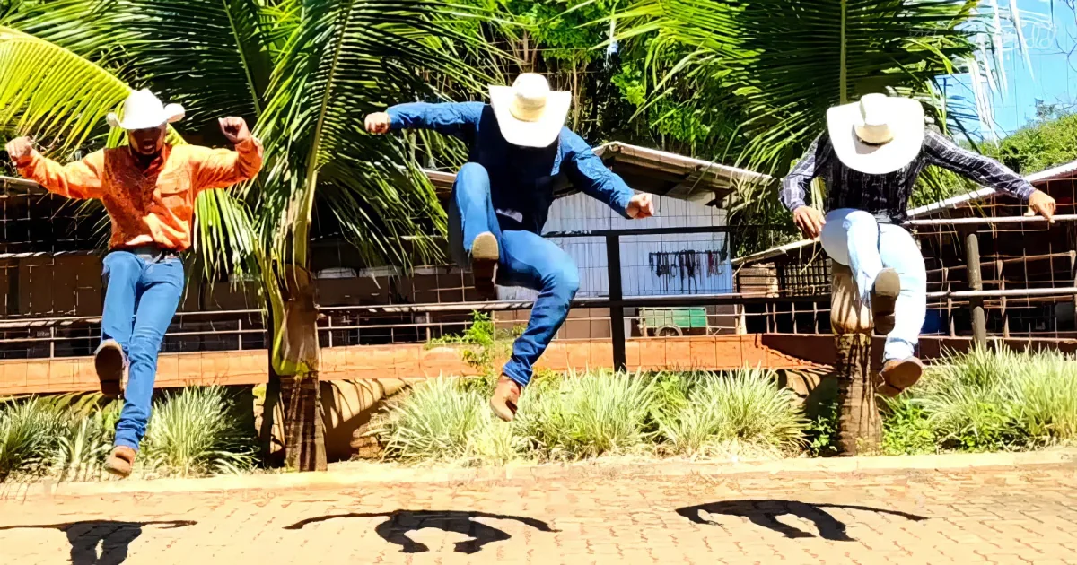 Three men in cowboy hats and jeans jump mid-air, casting shadows on a brick path.