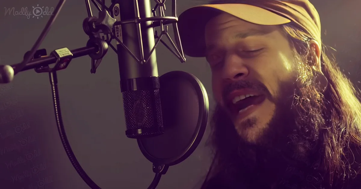 A man with long hair and a beard sings into a microphone in a recording studio.