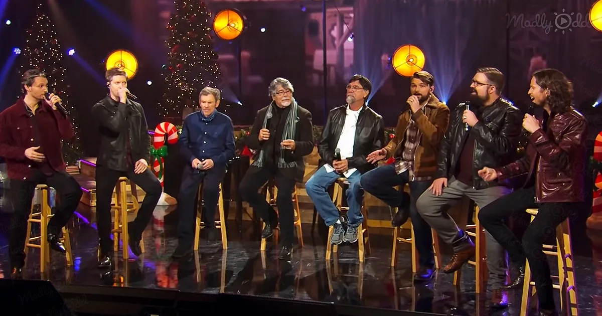 A group of people, some holding microphones, sit on stools on a stage with Christmas decorations.
