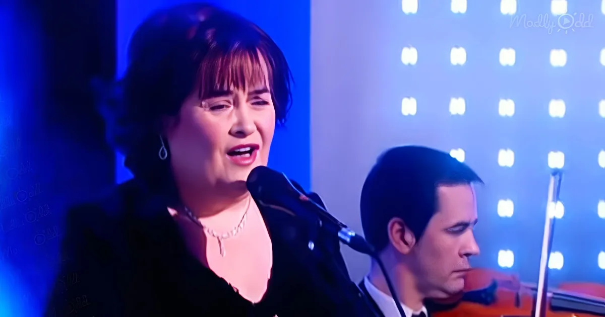A woman sings into a microphone on stage with a blue-lit background and a band.