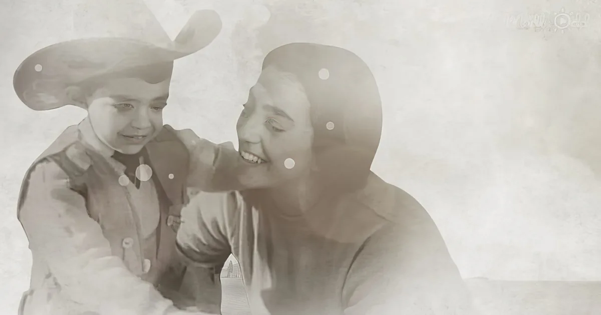 A child in a cowboy hat and vest is playfully interacting with an adult, both smiling.