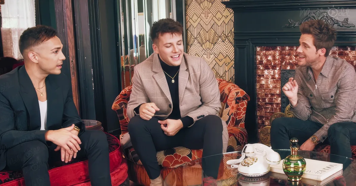 Three men in formal attire sit on patterned couches, engaged in conversation in a cozy, stylish room.