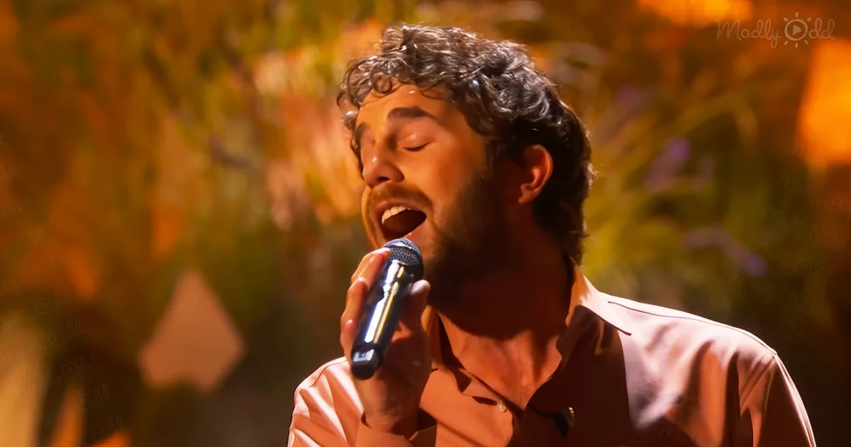 A man with curly hair and a beard sings passionately into a microphone.