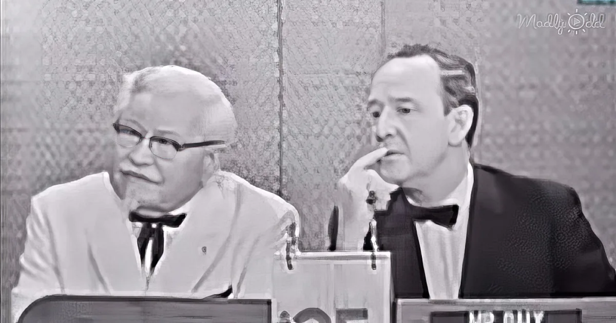 Two men in suits sit at a table, one gesturing while the other listens, in a formal setting.