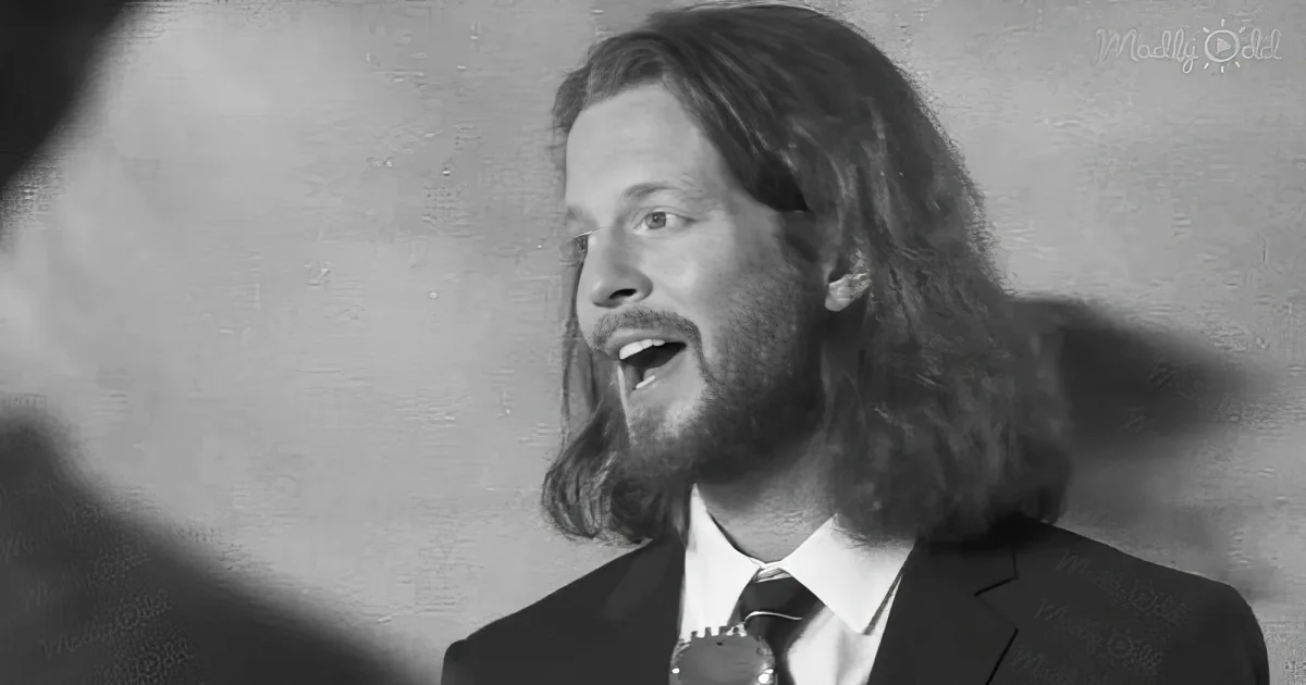 A man with long hair and a beard, wearing a suit, is singing into a microphone.