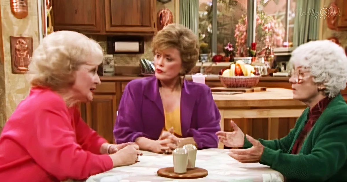 Three women in a kitchen setting, engaged in conversation, with a table and cups visible.