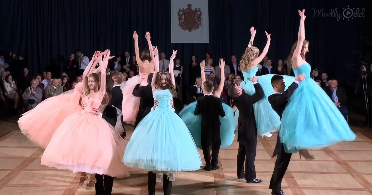 Dancers in pink and blue dresses perform a synchronized routine on a stage.