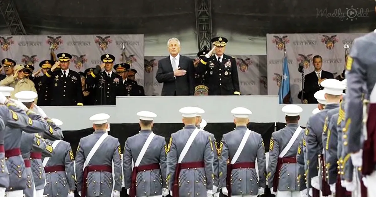 A man in a suit stands at a podium addressing a group of uniformed military personnel.