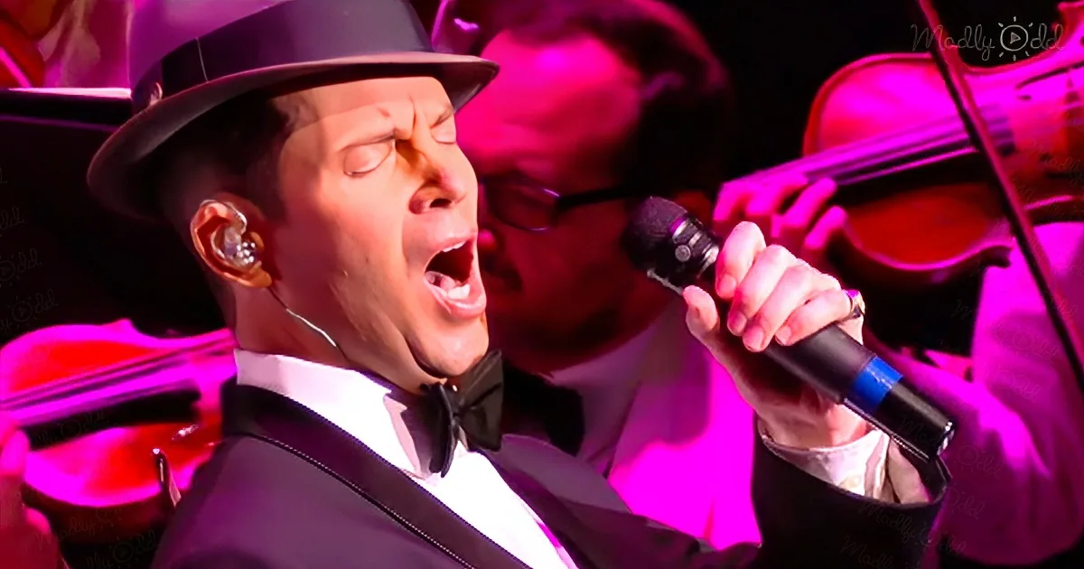 A man in a tuxedo and hat sings passionately into a microphone, surrounded by musicians.