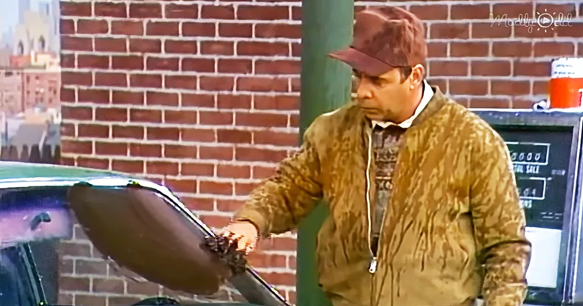 A man in a brown jacket and cap is holding a stroller in front of a brick wall.