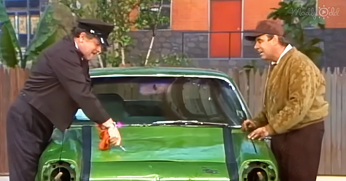 A man in a suit leans into a green car, interacting with another man in a brown jacket.