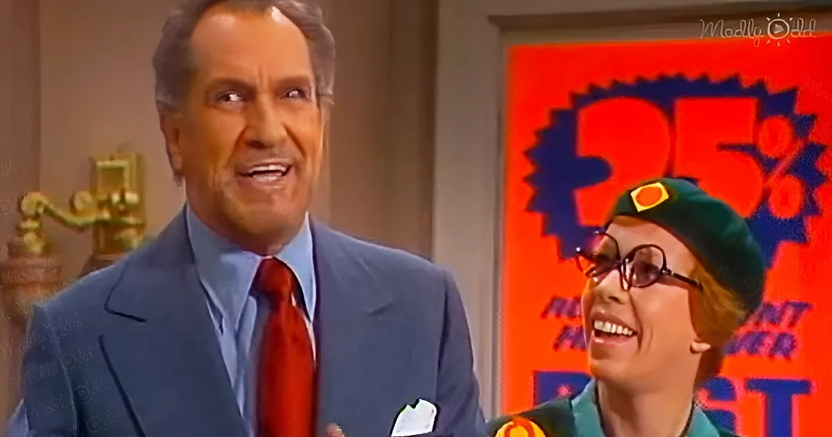 A man in a suit and tie smiles, with a woman in a green outfit and hat laughing beside him.