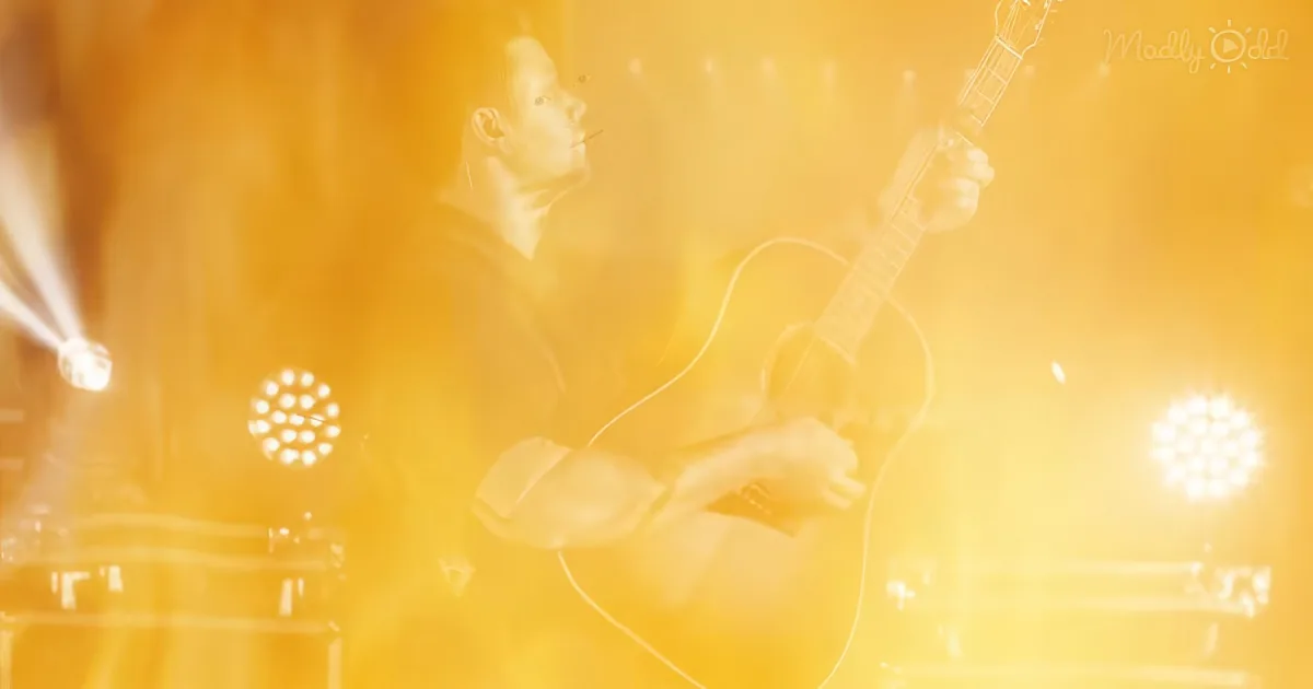 A musician plays guitar on stage with bright yellow lighting and blurred background.