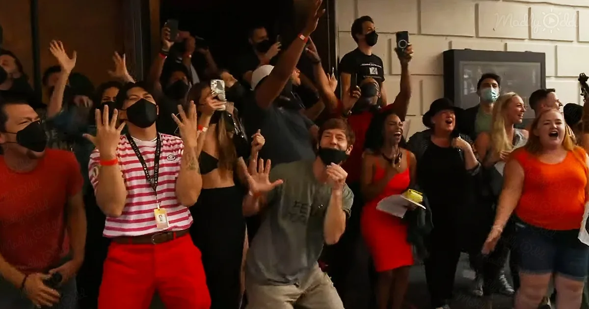 A group of people, some wearing masks, are cheering and raising their hands in excitement.