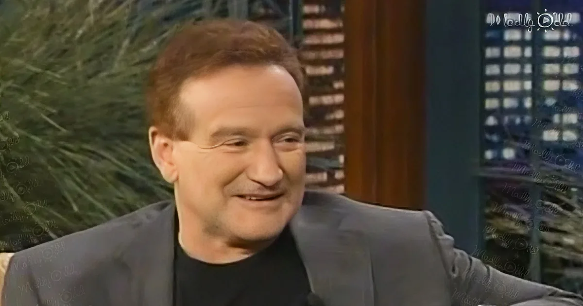 A smiling man in a suit and black shirt, likely on a talk show set with a cityscape background.
