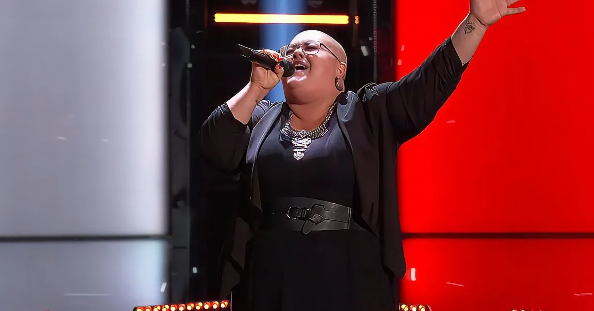 A person in a black outfit sings passionately on stage with a microphone, raising one arm.