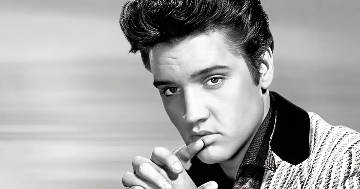 Elvis Presley, iconic figure, with signature pompadour hairstyle, holding hand near mouth, in black-and-white portrait.