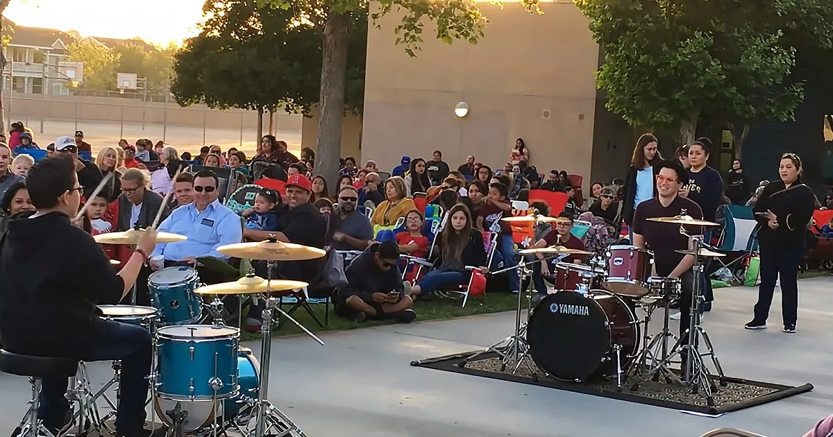 A drummer plays in front of a crowd at an outdoor concert.