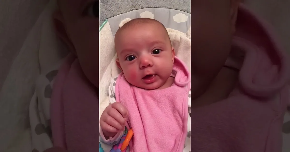 A joyful baby in a pink outfit smiles widely, showing a happy expression.