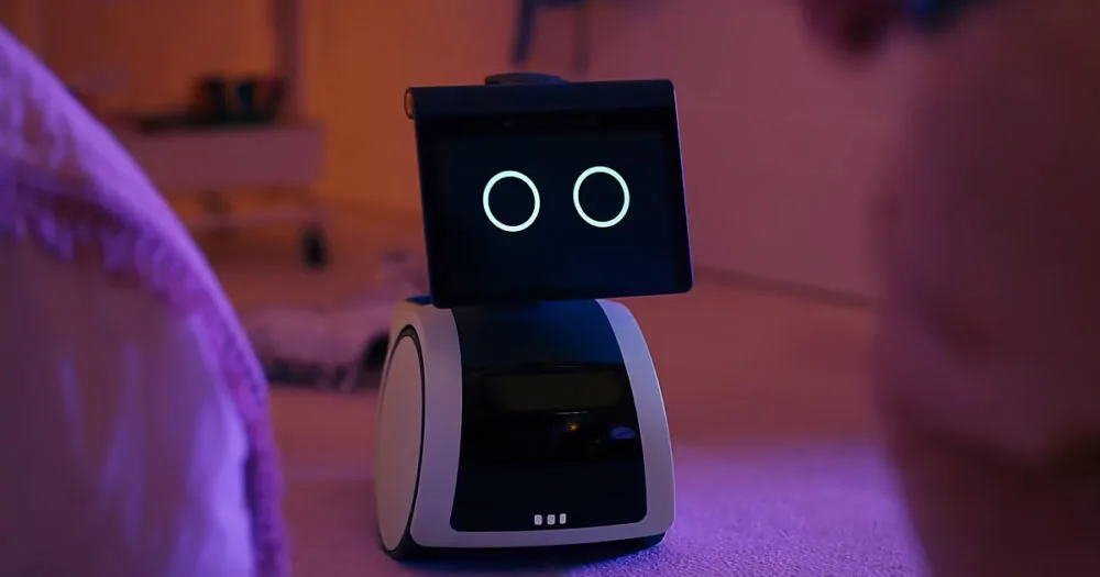 A small robot with glowing eyes sits on a bed, illuminated by purple light.