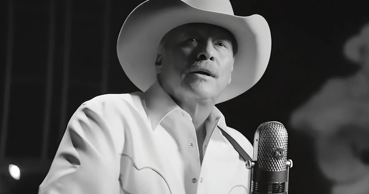 A man in a white shirt and cowboy hat sings into a microphone.