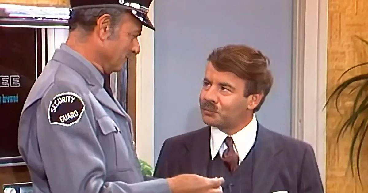 A security guard in uniform interacts with a man in a suit, both indoors.