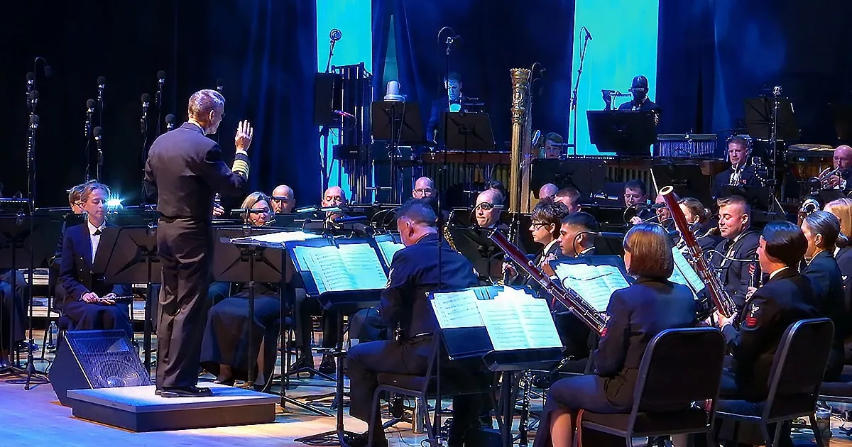 Conductor leads orchestra on stage with musicians and sheet music.