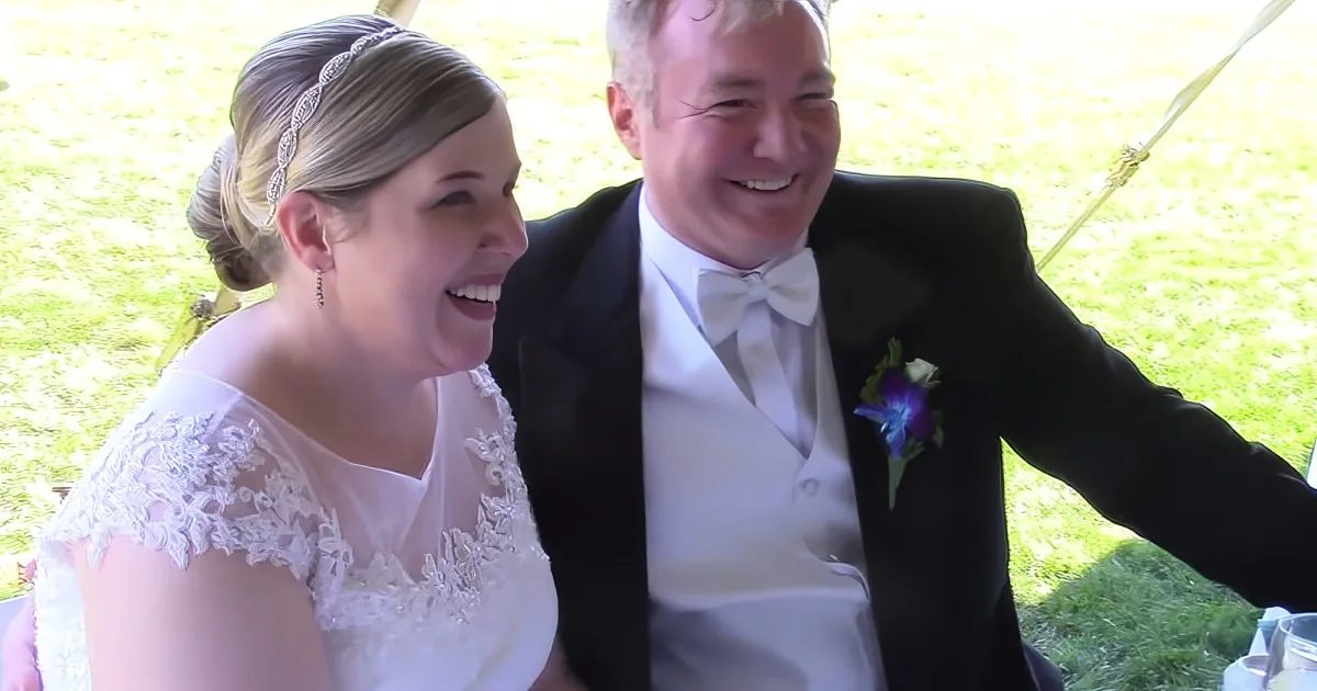 A bride and groom share a joyful moment, the bride in a white dress and the groom in a tuxedo, both smiling.