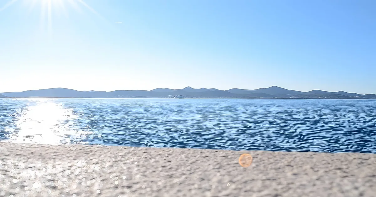 A serene view of a calm sea with distant mountains under a bright blue sky.