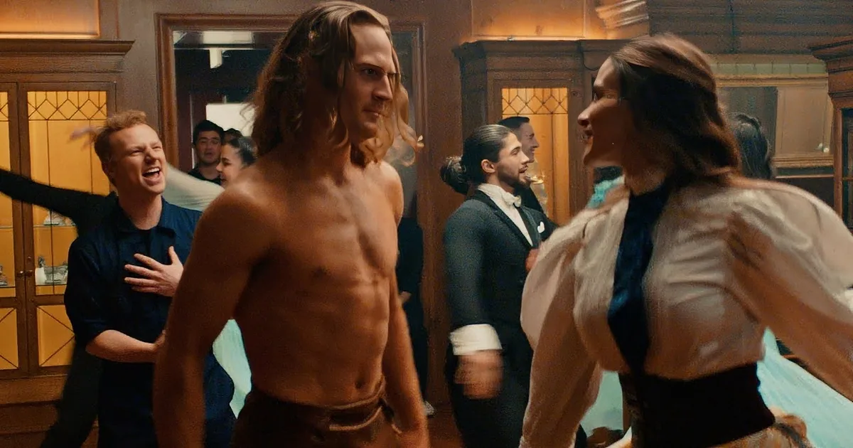 A shirtless man in brown shorts dances with a woman in a white blouse and yellow skirt, surrounded by a group of...