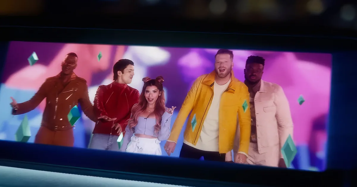 A group of five people in colorful outfits stands on a stage with a vibrant background.