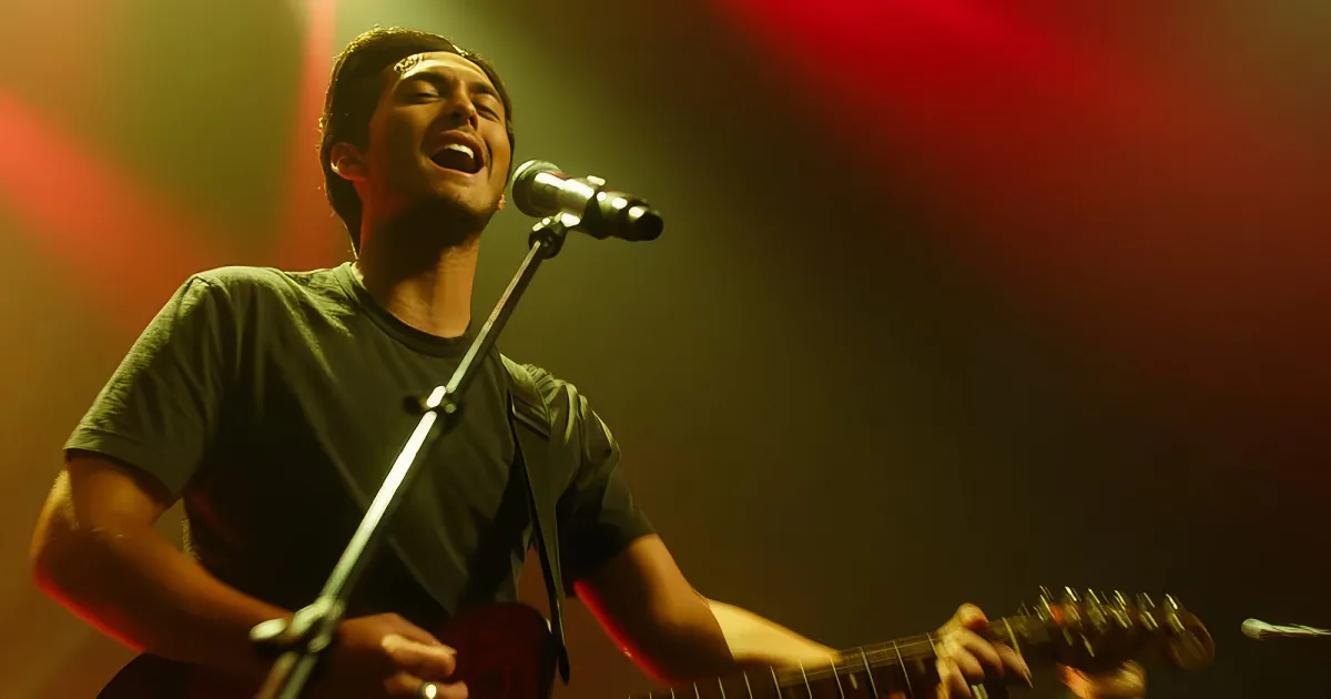A person singing into a microphone while playing a guitar on stage with red and green lighting.