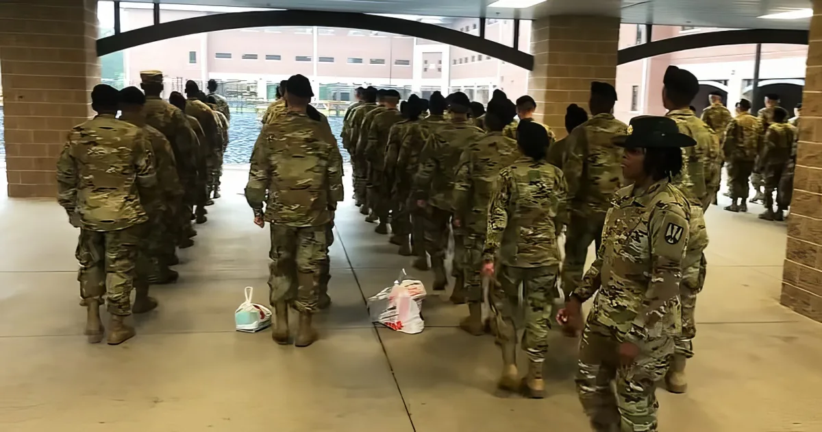 Soldiers in camouflage uniforms march in formation through a building.