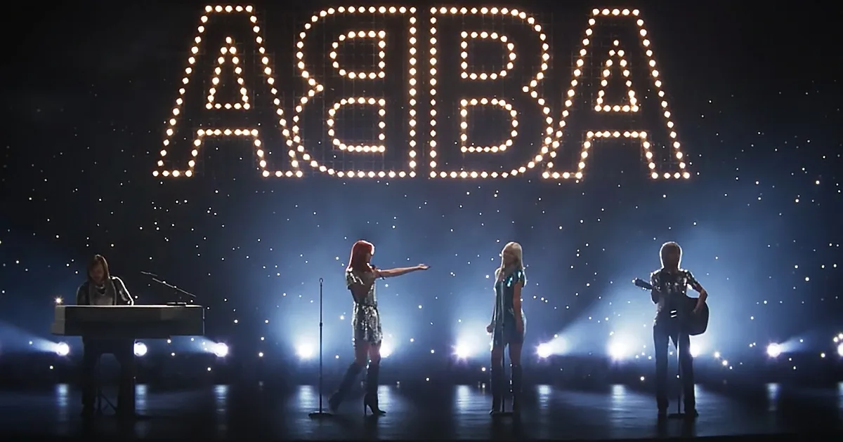 ABBA band performing on stage with large illuminated "ABBA" sign and spotlights.