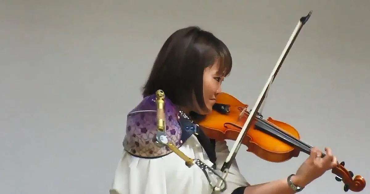 A person in a white dress plays a violin with a purple and gold shoulder accessory.