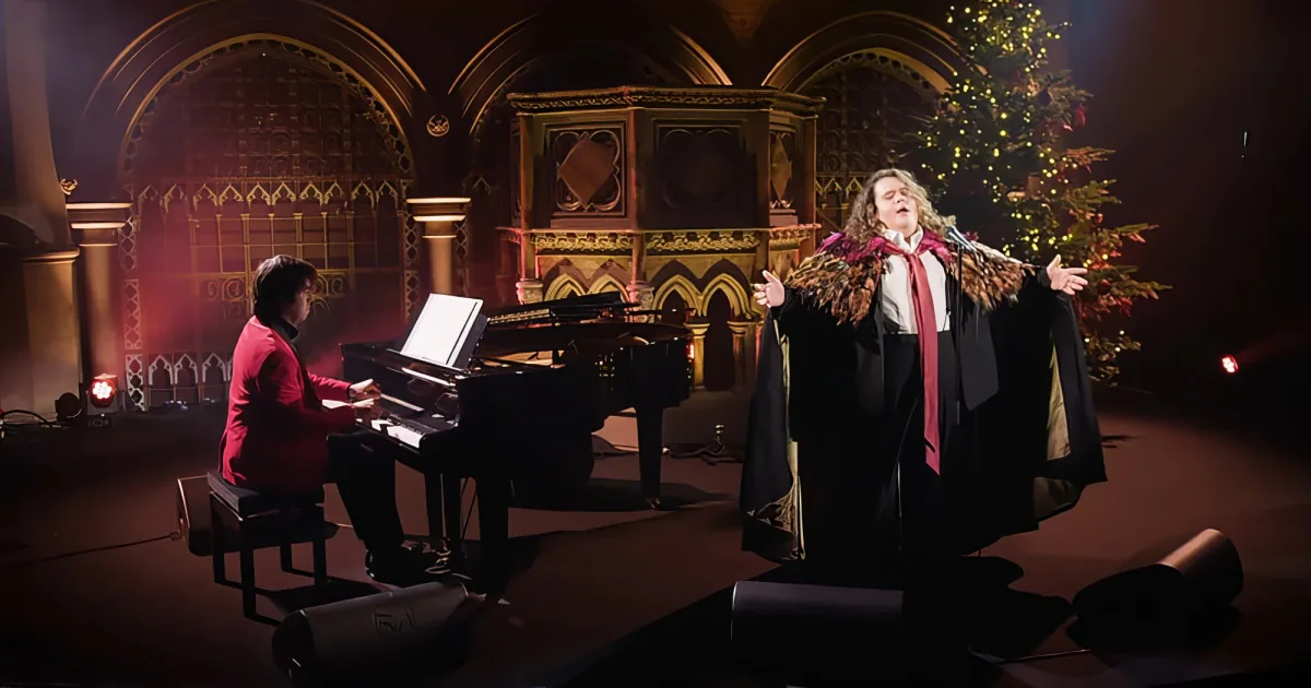 A pianist and a singer perform in a dimly lit church with a Christmas tree in the background.