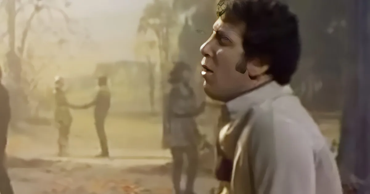 A man in a white shirt appears to be singing or speaking, with a blurred background of people and trees.