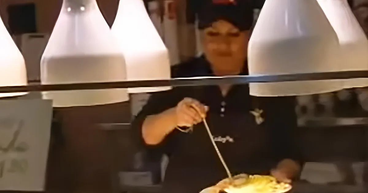 A person in a black uniform is behind a counter, preparing food with a smile.