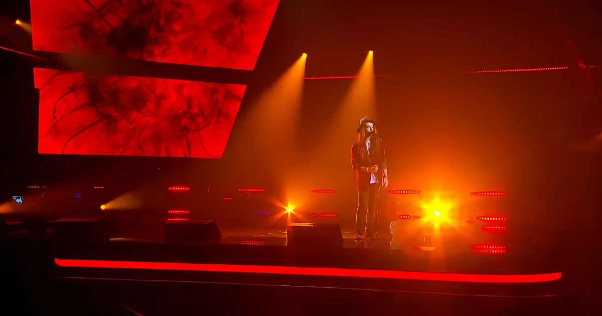 A person stands on a stage with red lighting and screens displaying abstract images behind them.