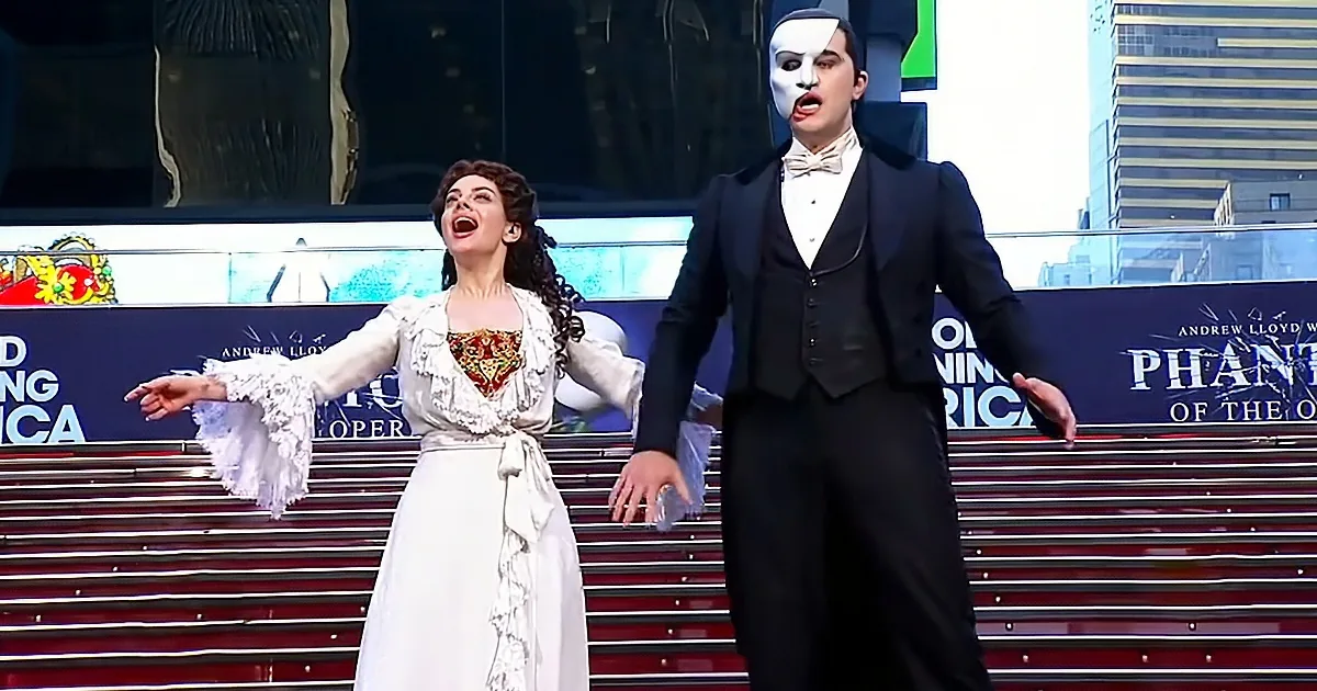 A woman in a white dress and a man in a black suit with a mask perform on a stage.