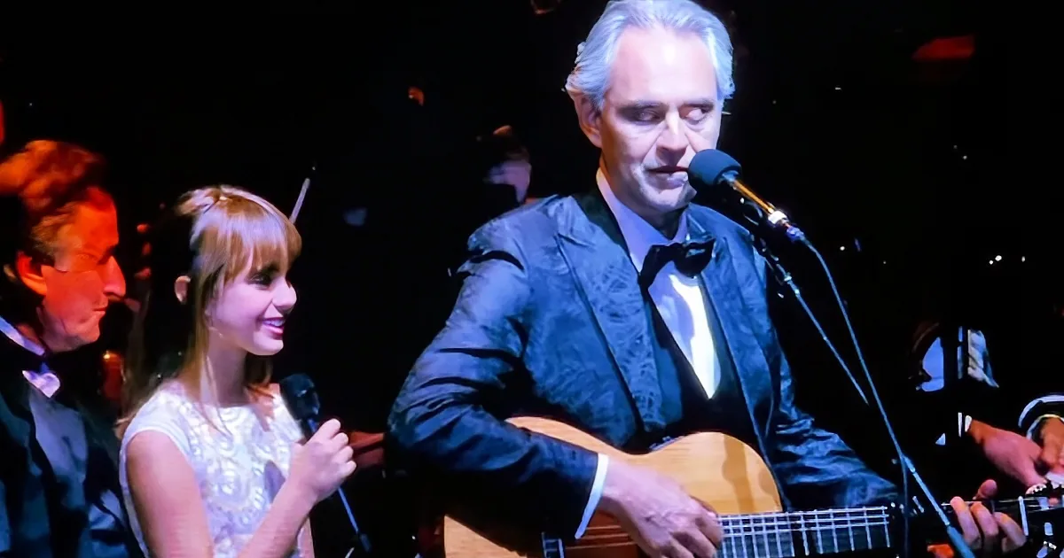 A man in a suit plays guitar and sings into a microphone on stage.