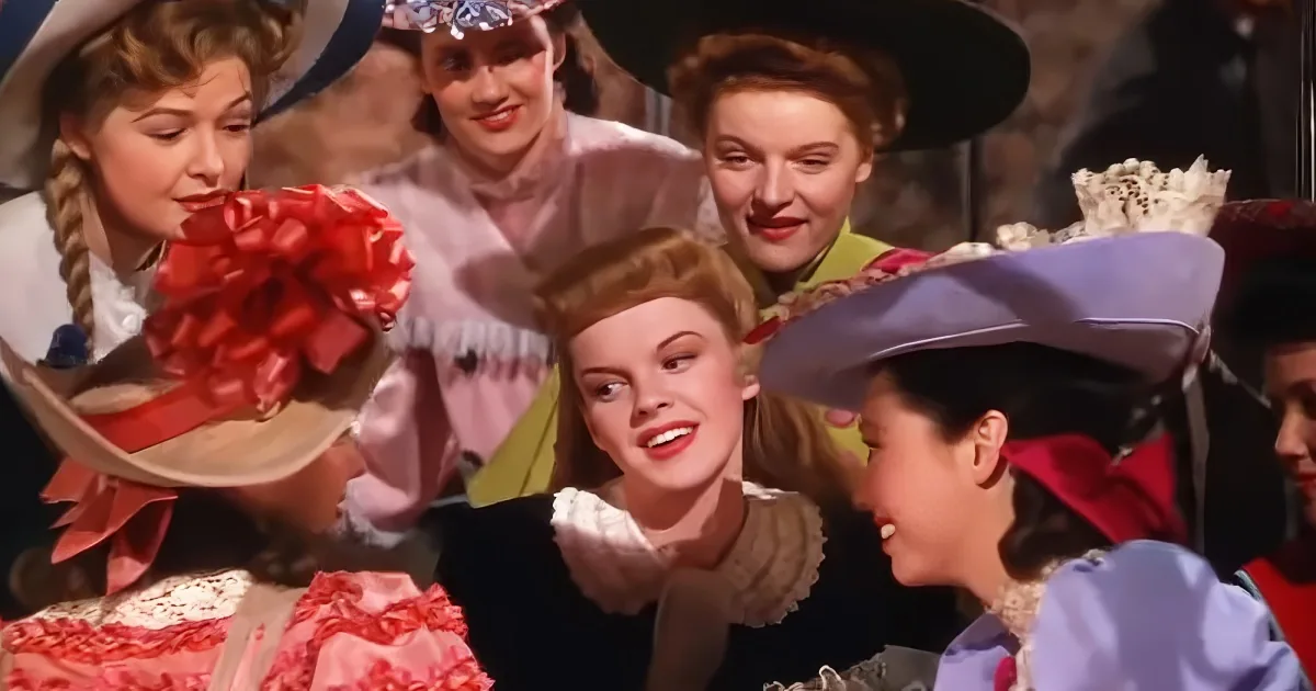 A woman in a red dress and cowboy hat is surrounded by other women in vintage attire, all smiling and interacting.