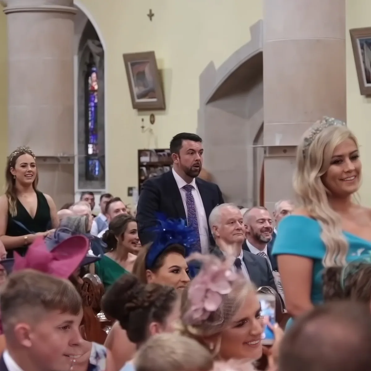 A man in a suit stands amidst a crowd of people in a church setting, surrounded by decorative elements.