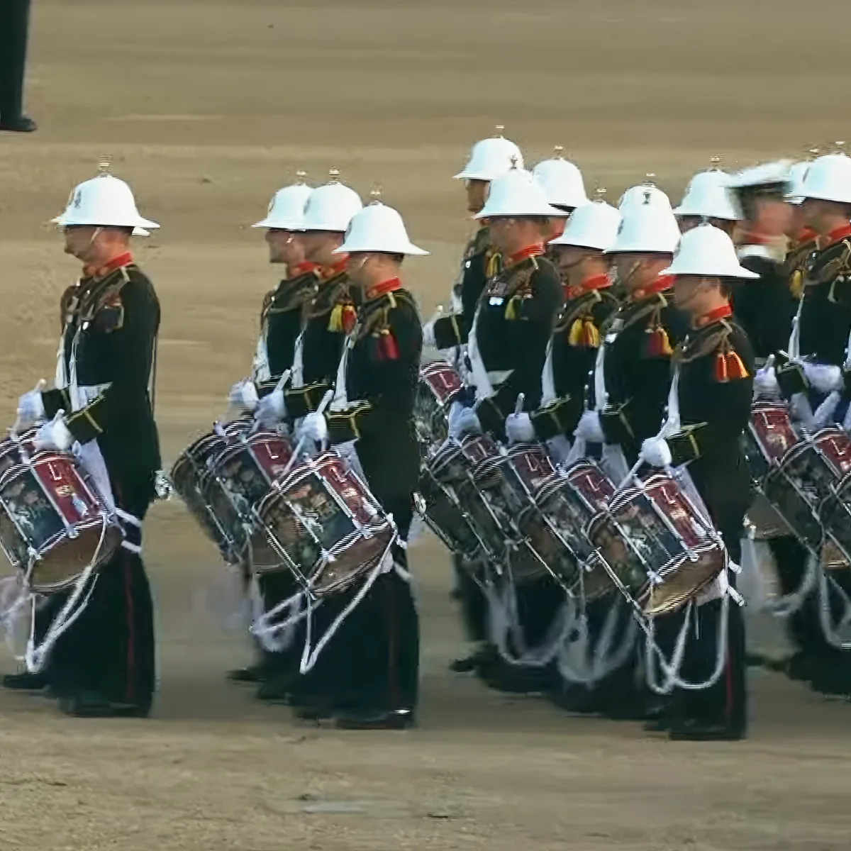 A group of uniformed drummers in white helmets and black uniforms marching in formation.